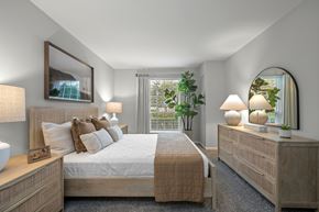 Oakbrook Terrace apartment for rent - A well-lit bedroom with a large bed, a nightstand with a lamp, and a mirror on the wall.