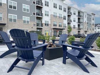 A patio with blue chairs and a fire pit in front of an apartment building