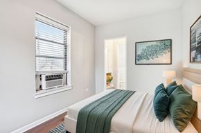Chicago apartment for rent - A bedroom with a bed, a window with blinds, a lamp, and a painting on the wall.
