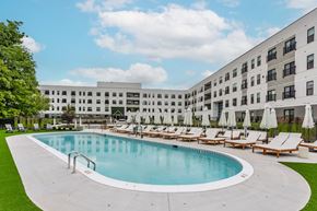 Cincinnati apartment for rent - A large swimming pool surrounded by sun loungers and umbrellas in front of a modern building.