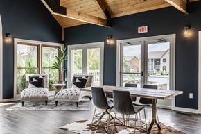 Westerville apartment for rent - A community clubhouse featuring two cozy comfy chairs, a table surrounded by chairs, hardwood-style flooring, and large windows.