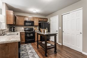 Reynoldsburg townhouse for rent - A kitchen with a kitchen island, black appliances, granite countertops, wooden cabinets, and hardwood-style flooring.
