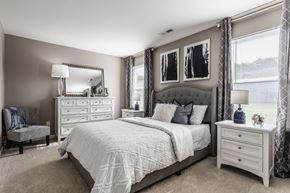 Reynoldsburg townhouse for rent - A furnished bedroom with carpeted flooring, stylish decor, and two windows for natural light.