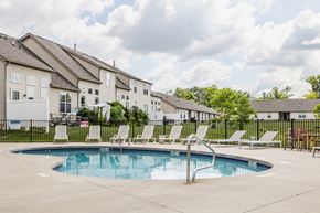 Reynoldsburg townhouse for rent - Swimming pool with white lounge chairs and a black fence, with apartment buildings in the background.