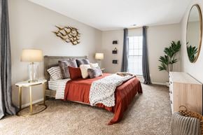 Westerville apartment for rent - A bedroom at Fairway Lakes with a queen-sized bed, carpeted flooring, stylish decor, and a window.