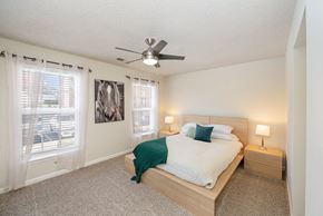 Lexington apartment for rent - A spacious bedroom with carpeted flooring, a bed with an end table on each side, and two windows.