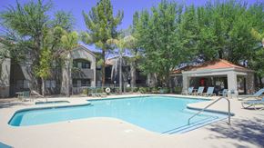 Tucson apartment for rent - A swimming pool surrounded by trees and a building in the background.
