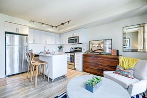 Seattle apartment for rent - A modern kitchen with a white fridge, a white dining table with chairs, a white sofa with a yellow pillow, and a wooden cabinet.
