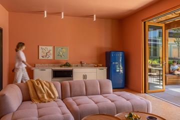Seattle apartment for rent - A woman is walking in a living room with a pink couch and a blue refrigerator.