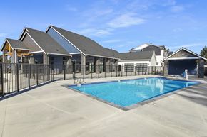 Lacey apartment for rent - A large swimming pool is surrounded by a black fence and a building with a grey roof.