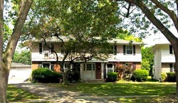 Tonawanda triplex for rent - A white house with a red door is surrounded by greenery.