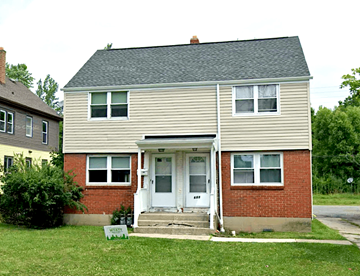 Buffalo triplex for rent - A two-story house with a white door and a sign in front that says "For Sale".