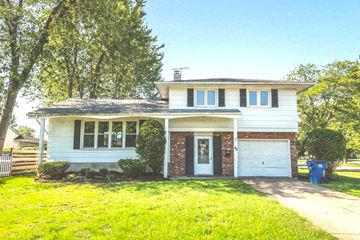 Amherst townhouse for rent - A white house with a black garage door is surrounded by green grass and trees.