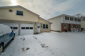 Amherst triplex for rent - A blue car is parked in front of a tan house with a white garage door.