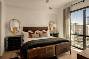 Nashville apartment for rent - A bedroom with a large bed, two lamps, and a view of the city.