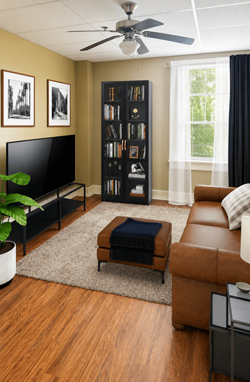 Little Rock apartment for rent - A living room with a brown leather couch, a black television, a brown ottoman, a bookshelf, and a ceiling fan.
