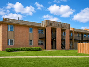 Bartlesville apartment for rent - A red brick building with a balcony and a green lawn in front.