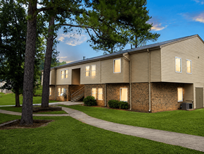 Rome apartment for rent - A building with a brown siding and a brick wall is surrounded by a grassy area and trees.