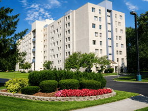 Ypsilanti apartment for rent - A large white building with a flower bed in front.
