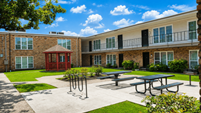 Houston apartment for rent - A sunny day at the courtyard of a brick building with a red entrance and a gazebo.