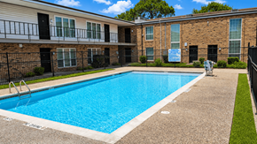 Houston apartment for rent - A swimming pool in front of a brick building with a sign that says "For Rent".