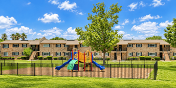 Jacksonville apartment for rent - A playground with a slide and a tree in front of a building.