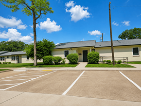 Alexandria apartment for rent - A parking lot in front of a building with a tree and bushes.