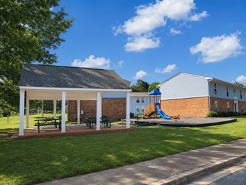 Thomaston apartment for rent - A playground area with a slide and picnic tables is located in front of a building.