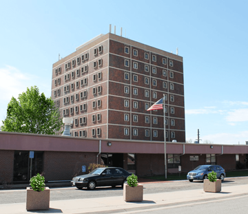 Denver apartment for rent - a tall brick building with an flag in front of a parking lot