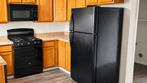 Socorro townhouse for rent - A black refrigerator stands in a kitchen with wooden cabinets and a black stove.