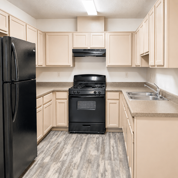 El Paso apartment for rent - A black fridge stands next to a black stove in a kitchen with wooden cabinets.