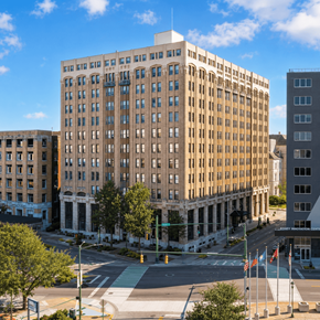 Chattanooga apartment for rent - A large, beige building with many windows is in the foreground of a city street.