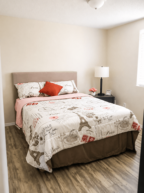 El Paso apartment for rent - A bed with a white comforter and a pink pillowcase is in a room with a lamp and a picture frame on a nightstand.