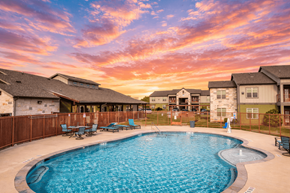 Bastrop townhouse for rent - A swimming pool surrounded by a wooden fence and benches with a sunset in the background.