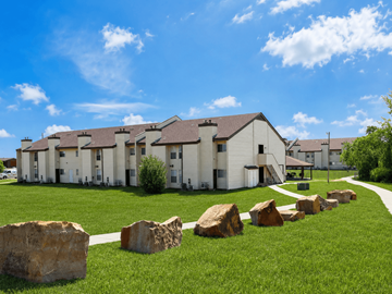Tulsa apartment for rent - A row of houses with a grassy front yard and large rocks in the foreground.