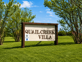 Tulsa apartment for rent - A sign that says Quail Creek Villa stands in a grassy field.