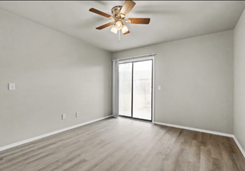 An empty living room with a ceiling fan and a sliding glass door