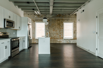 An empty kitchen with white cabinets and appliances and a exposed brick wall