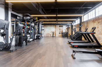 A gym with cardio machines and weights on a wooden floor