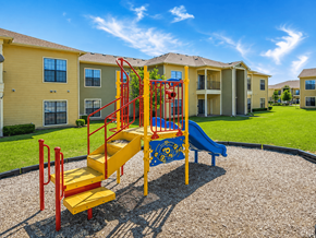 Cleburne townhouse for rent - A playground with a yellow slide and red railings in front of apartment buildings.
