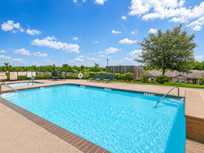 Conroe apartment for rent - A large blue swimming pool surrounded by a fence and trees.