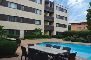 St. Louis apartment for rent - Poolside table and chairs are set up outside a building.