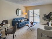 Quincy apartment for rent - A living room with a blue couch, grey armchairs, a glass table, and a round mirror on the wall.