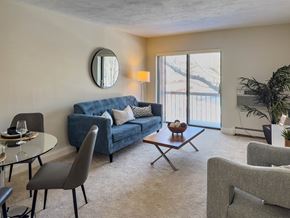Quincy apartment for rent - A living room with a blue couch, grey armchairs, a glass table, and a round mirror on the wall.