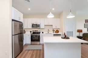 Somerset apartment for rent - Staged kitchen featuring white cabinetry, stainless appliances and a breakfast island topped with decorative pottery under two modern pendants.