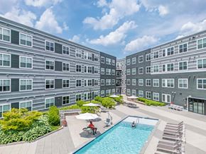 Billerica apartment for rent - A large swimming pool surrounded by lounge chairs and umbrellas in the middle of a courtyard at The Val
