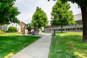 A sidewalk in front of a building with trees and a statue