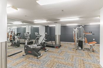 A gym with treadmills and other exercise equipment in a room with gray walls