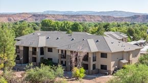 Cottonwood apartment for rent - A large building with a grey roof is surrounded by trees and bushes.