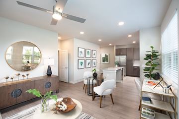 Houston apartment for rent - A modern living room with a round mirror, a dining table with chairs, and a kitchen area in the background.